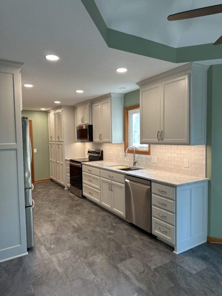 Galley kitchen with painted custom cabinets, tile backsplash, quartz countertops, and LVT flooring