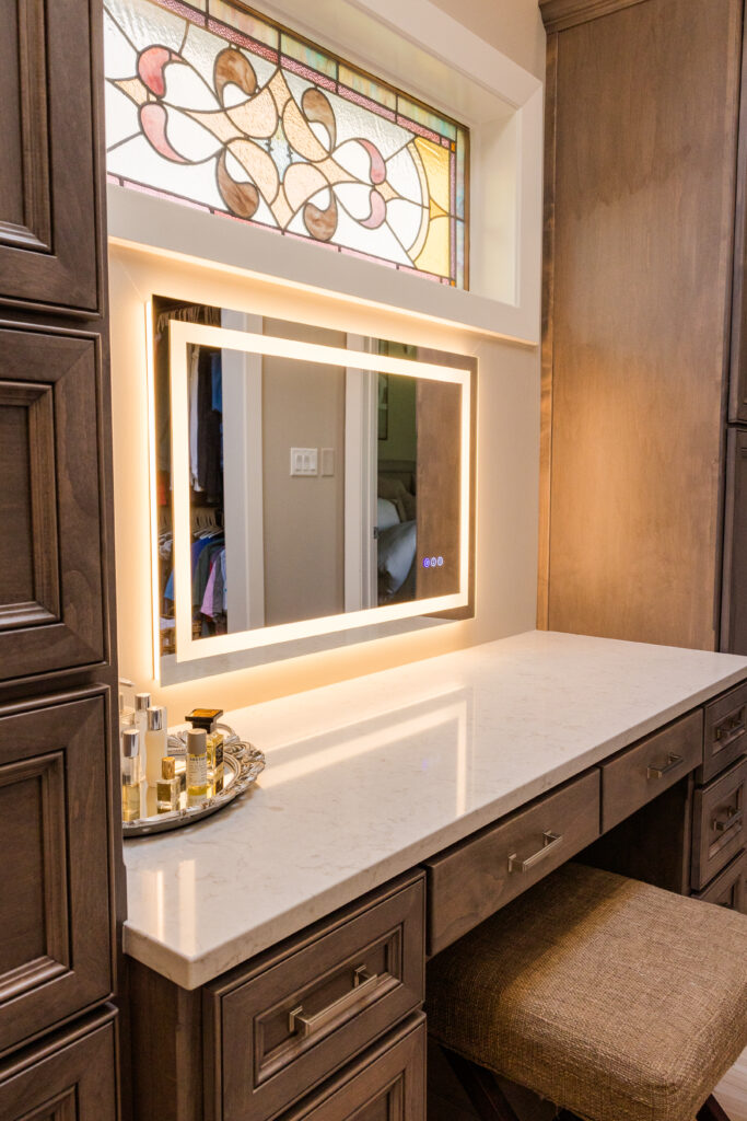 Primary bathroom vanity seating area with LED mirror and stained glass accent window